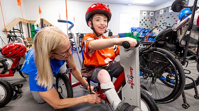 Caregiver helping a little boy on a bike.