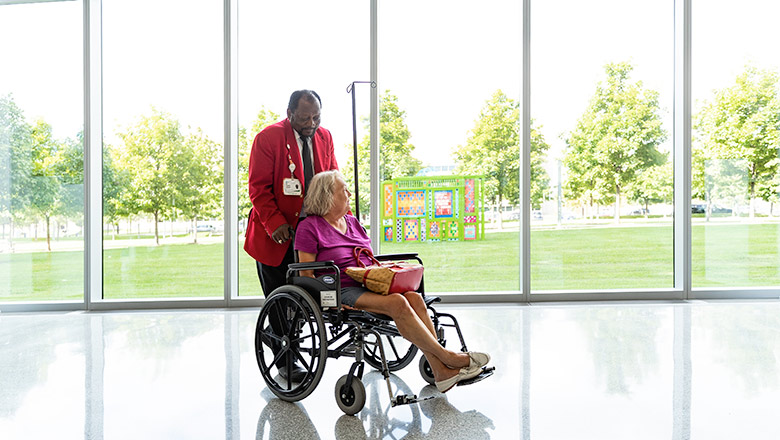 A Cleveland Clinic Red Coat aiding a patient in a wheelchair.